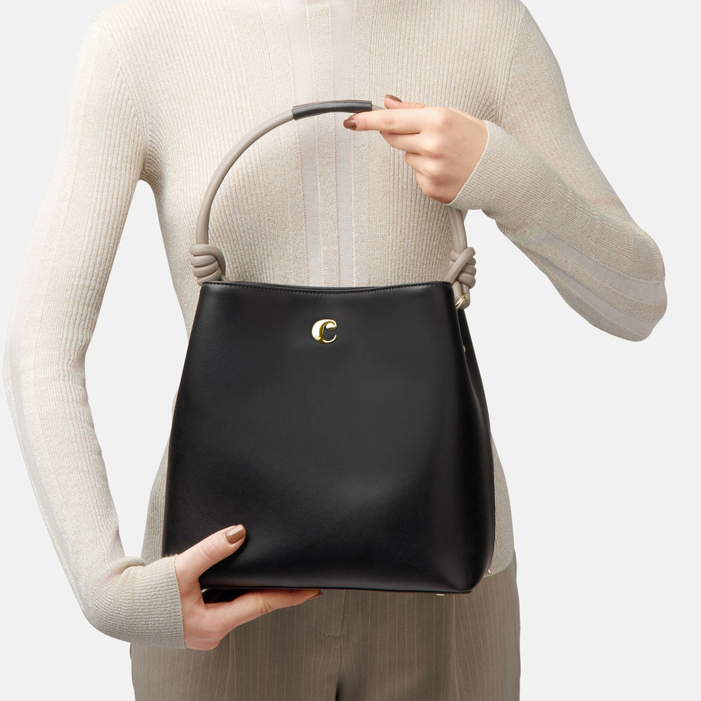 Person holding a black handbag with a Cacharel gold clasp against a neutral background