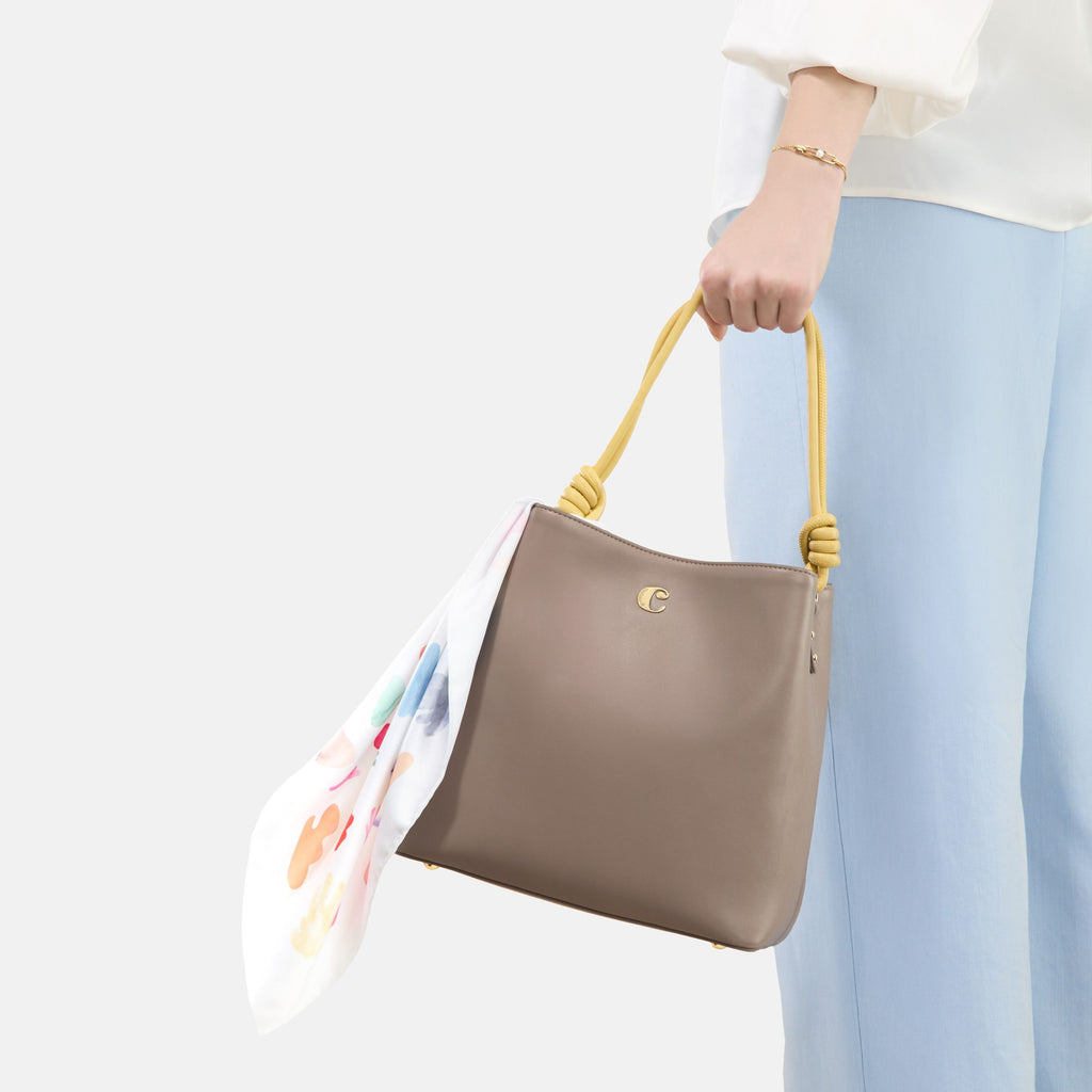 Person holding a brown Cacharel handbag with yellow handle against a white background