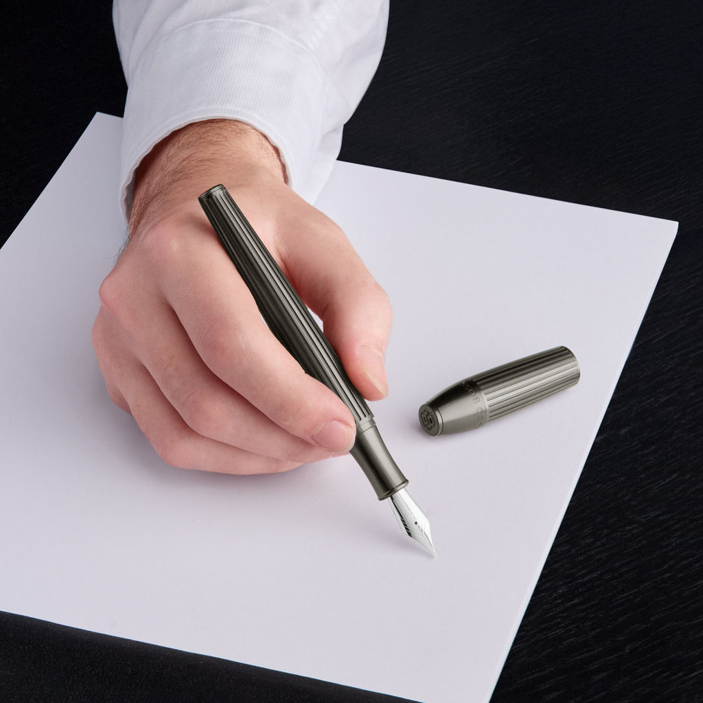 Hand holding a metallic BOSS fountain pen over a piece of paper with the cap beside it.
