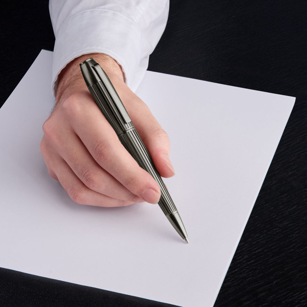 Hand holding a HUGO BOSS pen poised over a piece of paper on a black surface