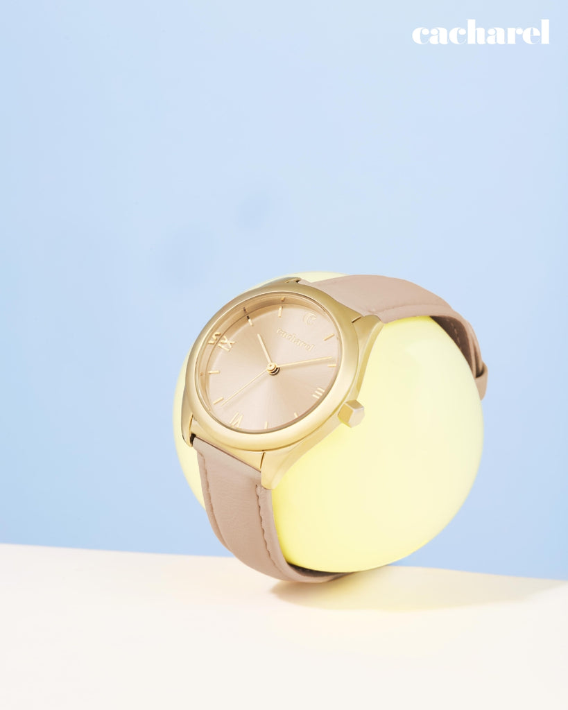 Cacharel gold and beige watch on a light blue background with 'cacharel' logo